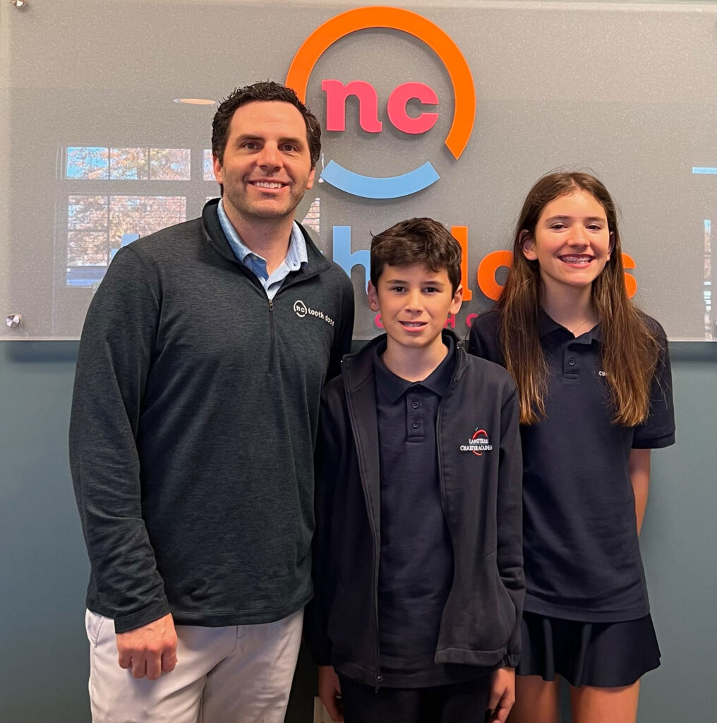 Dr. Jonathan Wells smiling with two children in front of the NC Tooth Docs logo
